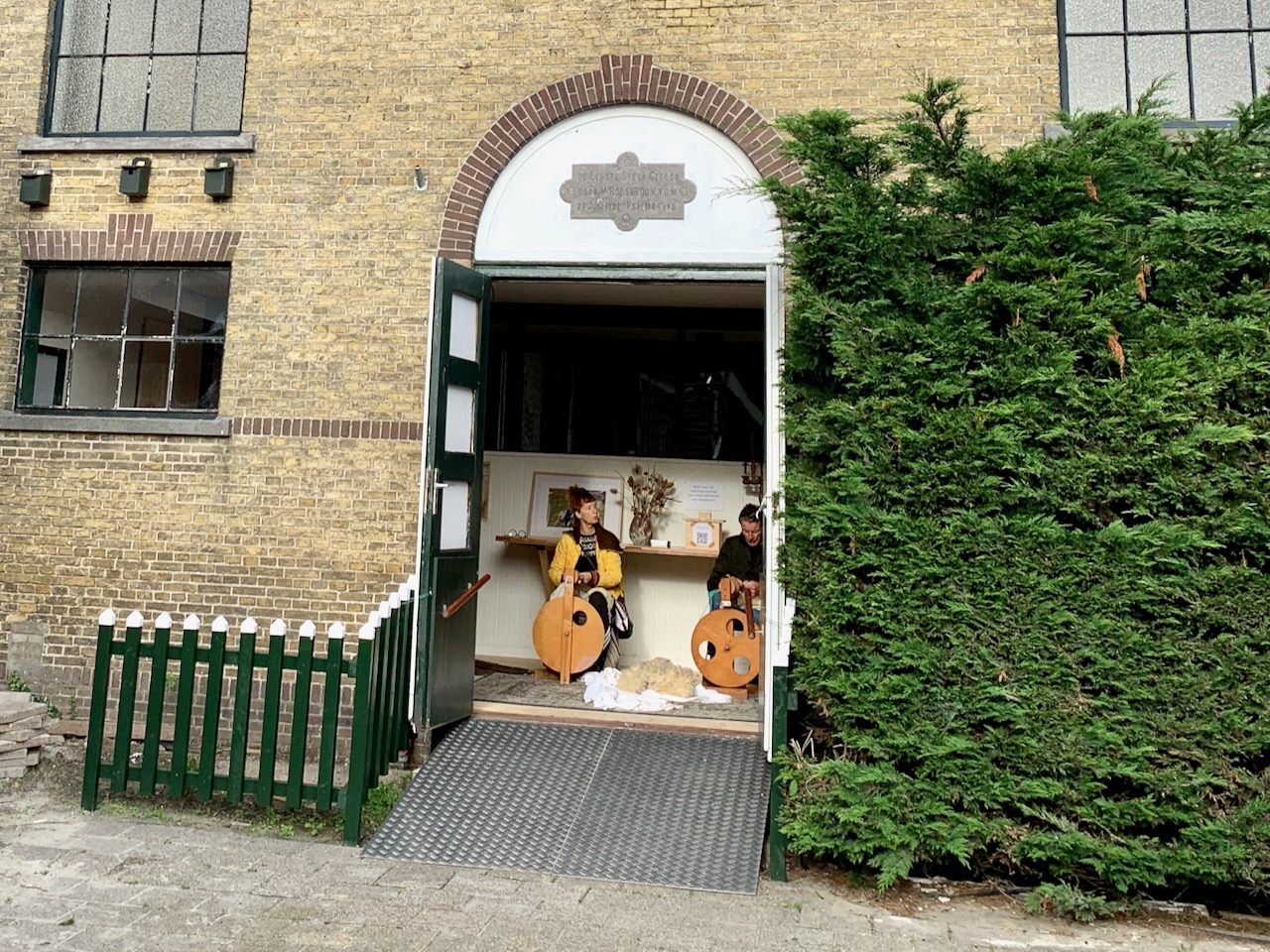 Die Holztüren der ehemaligen reformierten Kirche in Oosterend - geöffnet und darin zwei Personen am Spinnrad.
