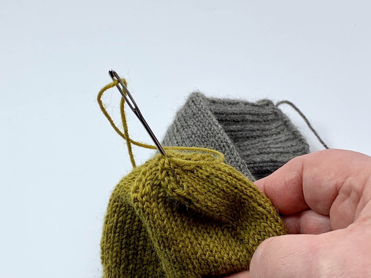 Die Nadel mit dem Restfaden wird durch die Mitte der Spitze nach  innen geführt, wo er vernäht wird.