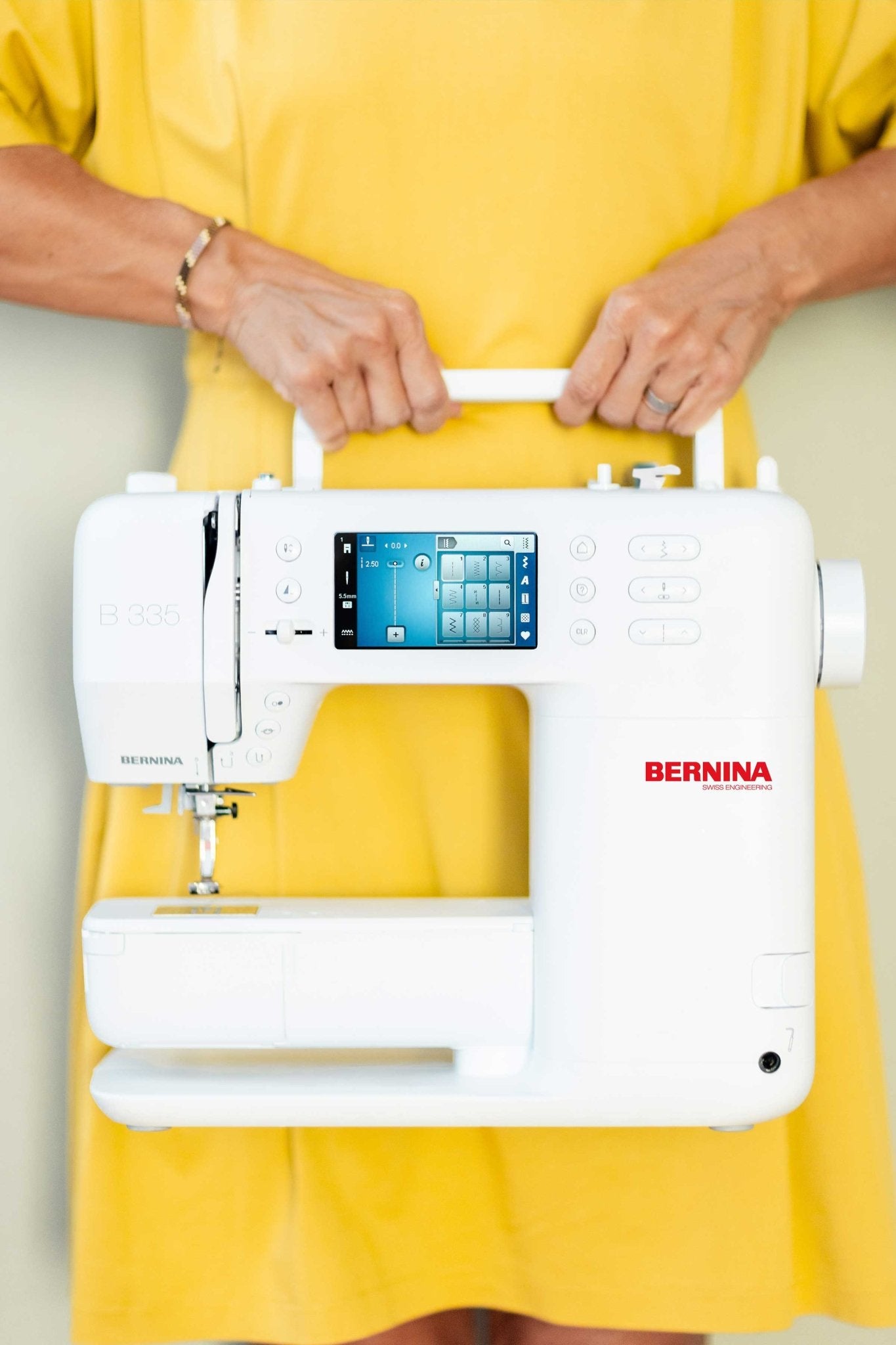 Eine Person im gelben Kleid trägt die kompakte BERNINA 335 am Tragegriff.